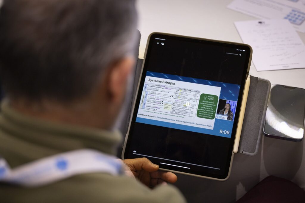 Over-the-shoulder view of an attendee following a session on a tablet showing the live slides and speaker feed