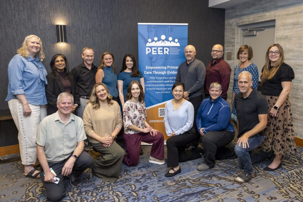 A posed group photo of roughly fifteen organizers and presenters gathered around the PEER banner